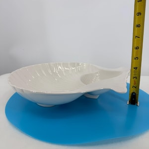 May include: A white ceramic serving dish in the shape of a seashell. The dish has a large, oval-shaped bowl with a smaller, separate compartment. The dish is approximately 8 inches long.