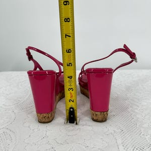 May include: Bright pink wedge sandals with cork soles and ankle straps. The wedge heel measures approximately 4 inches. The sandals are shown with a measuring tape.
