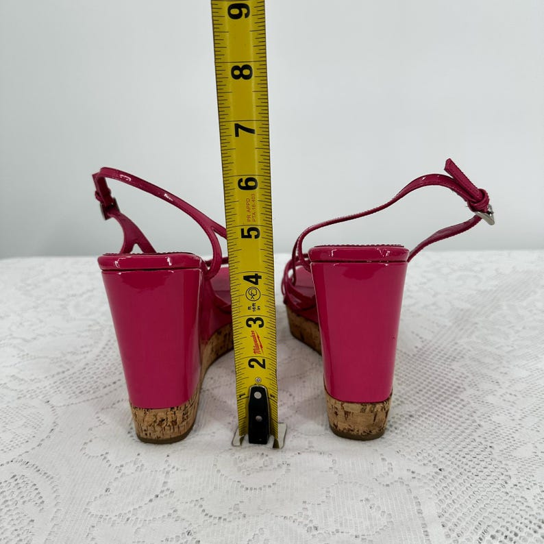 May include: Bright pink wedge sandals with cork soles and ankle straps. The wedge heel measures approximately 4 inches. The sandals are shown with a measuring tape.