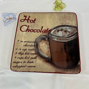 May include: Square ceramic plate with a hot chocolate recipe. The plate features a brown mug filled with hot chocolate and whipped cream. The text "Hot Chocolate" is written in a burgundy colour, along with the recipe.