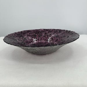 May include: A decorative bowl with a dark purple floral pattern on the inside and a textured gray exterior. The bowl has a wide, shallow shape, suitable for display or serving.