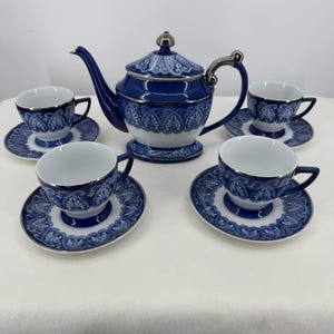 Puede incluir: Un juego de té compuesto por una tetera y tres tazas con sus platos a juego. Cada pieza está hecha de cerámica blanca con un patrón decorativo azul intenso que presenta intrincados adornos y bordes metálicos plateados en los bordes y asas.