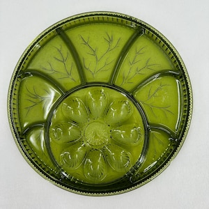 Peut inclure: Un plateau de service vintage en verre vert avec un motif floral au centre et des motifs de feuilles dans les compartiments. Le plateau rond a un bord festonné, idéal pour servir des collations ou des apéritifs.