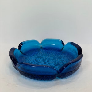 May include: A vibrant blue glass ashtray with a textured interior and a petal-like design. The ashtray is a deep shade of blue, with a textured surface in the center and smooth edges. A decorative piece for the home.