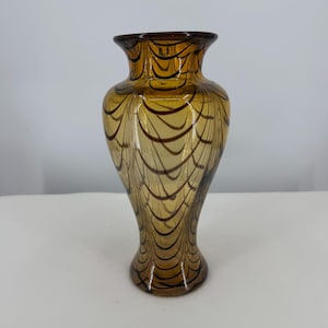 May include: A translucent amber glass vase featuring a flared rim and a narrow neck that widens toward the base. The surface is decorated with a repeating pattern of dark brown, thin, curved lines that create a delicate, web-like design.
