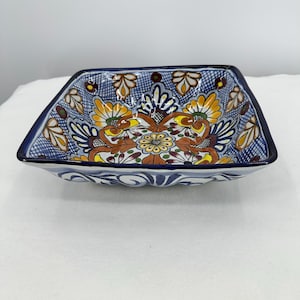 May include: Square ceramic bowl with a blue rim and intricate floral designs in yellow, orange, and brown. The bowl's interior features a detailed pattern against a blue background, showcasing a traditional aesthetic.