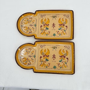 Op de afbeelding: Twee decoratieve keramische trays met een beige achtergrond en een gele rand. Elke tray heeft een halfronde en een rechthoekige sectie. De trays zijn versierd met een bloemen- en vogelontwerp in geel, rood en groen.
