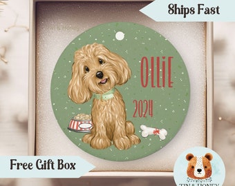 May include: A green round Christmas ornament with a cartoon illustration of a brown and white dog sitting next to a red and white dog bowl. The dog is wearing a green collar and the ornament says "Ollie 2024".