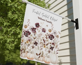 May include: A white garden flag with a floral and pumpkin design. The flag features the words "Thankful, Grateful, Blessed" and "Wilson Family" in black script. The design includes white pumpkins and flowers in shades of burgundy, yellow, and cream.