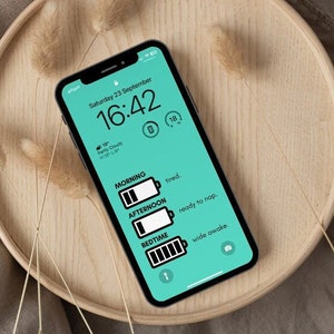 May include: A smartphone displaying a digital clock with the time 16:42 and the date Saturday 23 September. The screen also shows a battery icon with a low battery level and the words "Morning, tired." "Afternoon, ready to nap." and "Bedtime, wide awake."