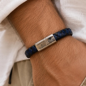 Peut inclure: Un bracelet tressé composé de brins de cuir bleu foncé et noir alternés. Le bracelet comporte un fermoir métallique rectangulaire de couleur argentée gravé avec le texte FOREVER & ALWAYS, un symbole de cœur et le prénom Katie.