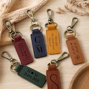 Peut inclure: Six porte-clés rectangulaires en cuir avec des mousquetons et des anneaux en métal bronze. Chaque porte-clés présente des textes et symboles gravés au laser, incluant des initiales, des dates, des coordonnées et des phrases comme Love You Forever.