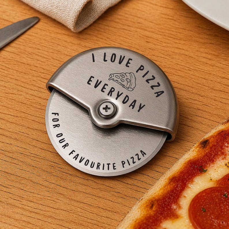 May include: A stainless steel pizza cutter with the words "I LOVE PIZZA EVERYDAY FOR OUR FAVOURITE PIZZA" engraved on it. The pizza cutter is next to a slice of pizza with pepperoni.