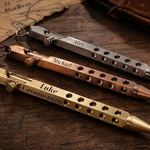 Könnte beinhalten: Drei Metall-Kugelschreiber mit einem sechseckigen Schaft, der eine Reihe kreisförmiger Aussparungen aufweist. Jeder Stift ist mit einem Namen graviert, darunter Alex, Michael und Luke Groomsman. Die Stifte haben silberne, kupferne und messingfarbene Oberflächen.
