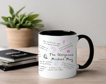 Può includere: Una tazza in ceramica bianca con bordo e manico neri. La tazza ha un design colorato con testo che recita "Le mie imperfezioni mi rendono unica e bella. Sono un faro di amore e positività. La magnifica tazza Mindset. Sono l'architetto del mio destino. Ogni ostacolo è un trampolino di lancio verso il successo. Credo nella mia intuizione e saggezza."