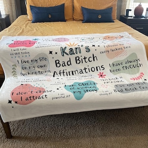 May include: White throw blanket with colorful abstract shapes and text that reads "Kari's Bad Bitch Affirmations". The text includes phrases like "I am a ray of fucking sunshine", "I don't chase, I attract", and "I am Queen of owning my story".