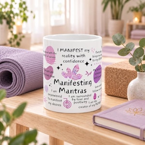 May include: A white ceramic mug featuring purple crystal illustrations and black text that reads "I MANIFEST my reality with confidence", "Manifesting Mantras", "I am empowered to manifest my desires", and "I am surrounded by love and positivity".