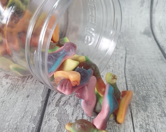 May include: A clear plastic jar labelled "SWEETS" with a variety of colourful gummy candies spilling out. The candies are shaped like fish and are in shades of pink, green, yellow, orange, and purple.