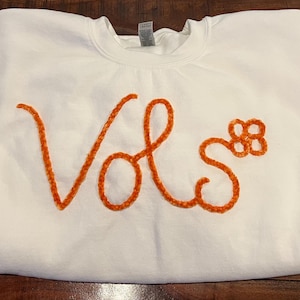 Puede incluir: Sudadera blanca con un diseño bordado en naranja "Vols".