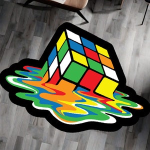 Puede incluir: Una alfombra colorida con un contorno negro presenta un cubo de Rubik derritiéndose con un efecto líquido arcoíris.
