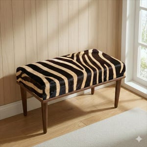 Puede incluir: Banco rectangular con tapa estampada de cebra y patas de madera marrón oscuro. El patrón de cebra presenta rayas negras y beige. El banco es un mueble decorativo, adecuado para una sala de estar o dormitorio.