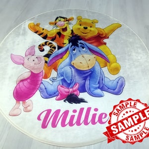 May include: A round white rug with a Winnie the Pooh theme. The rug features Winnie the Pooh, Tigger, Piglet, and Eeyore. The rug has the name "Millie" written in pink cursive letters. The rug has a red "SAMPLE" stamp on it.