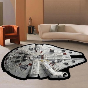 Peut inclure: Un tapis rond noir et blanc avec une image détaillée du vaisseau spatial Millennium Falcon de Star Wars. Le tapis est sur un sol beige clair dans un salon.
