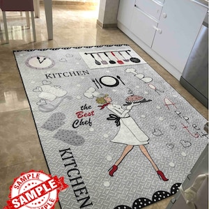 May include: A gray and black kitchen rug with a white chef illustration holding a pie. The rug has the words "Kitchen" and "The Best Chef" on it.