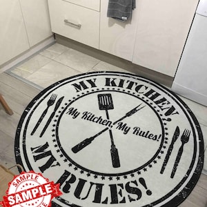 May include: A round white kitchen rug with black text that reads "My Kitchen, My Rules!" and a black and white illustration of crossed kitchen utensils. The rug has a distressed, vintage look.