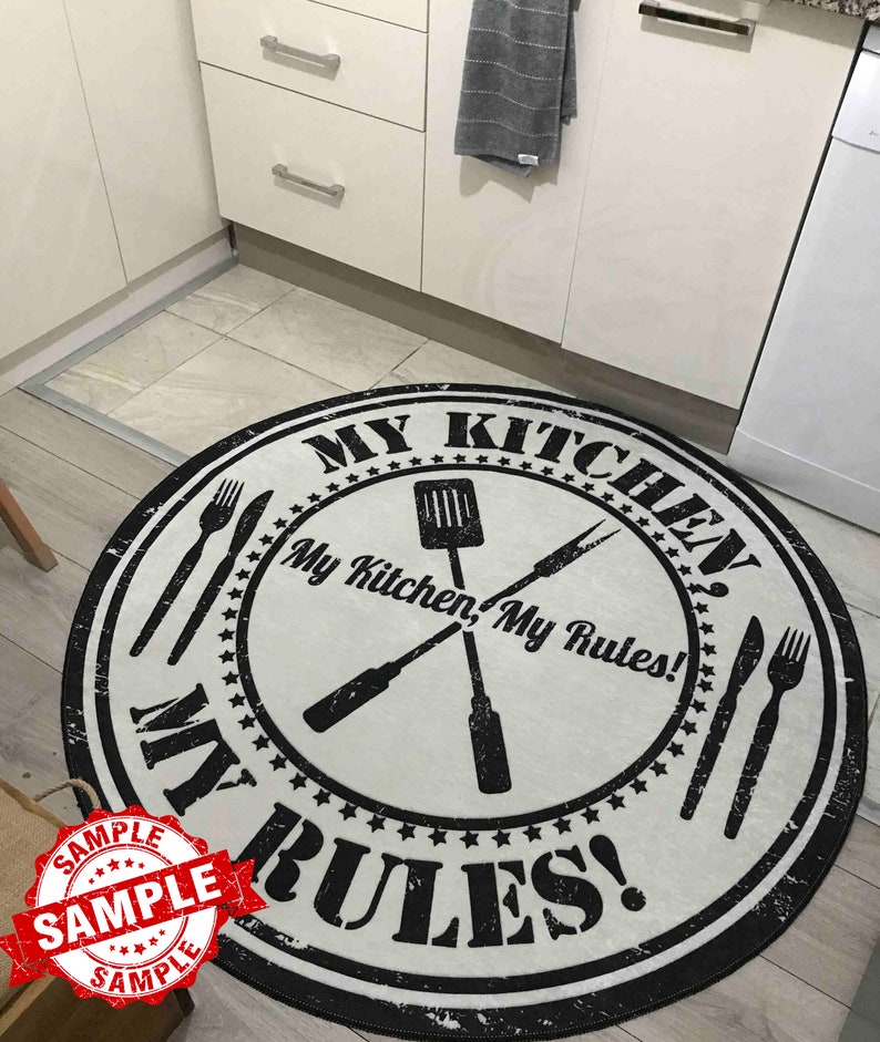May include: A round white kitchen rug with black text that reads "My Kitchen, My Rules!" and a black and white illustration of crossed kitchen utensils. The rug has a distressed, vintage look.