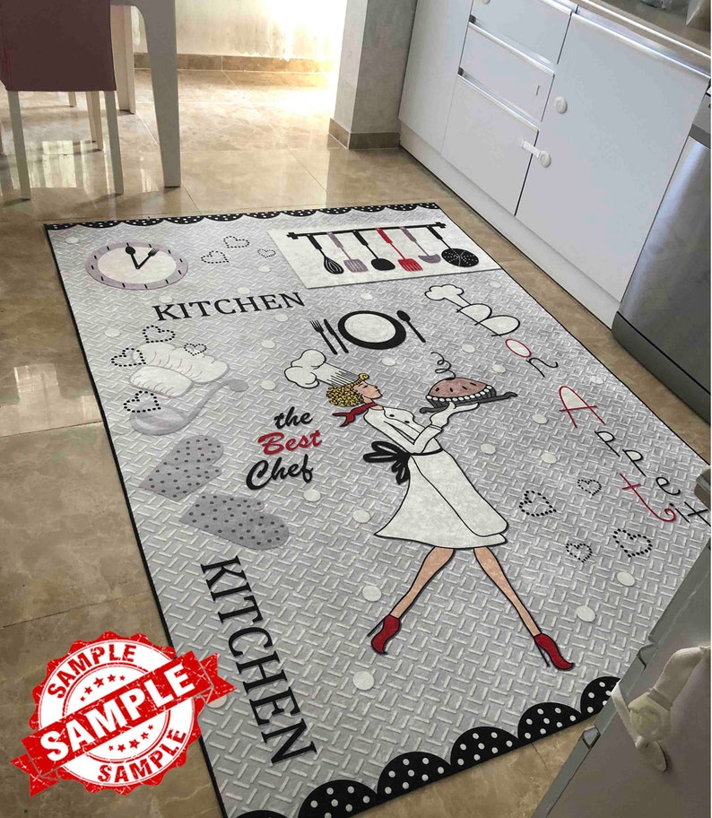 Op de afbeelding: Een grijs en zwart keukenkleed met een witte chef-kok illustratie die een taart vasthoudt. Het kleed heeft de woorden "Keuken" en "De beste kok" erop.