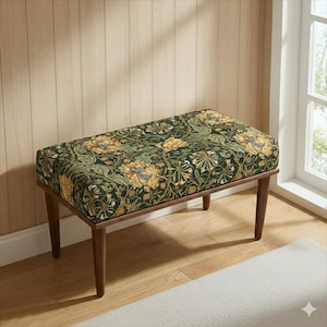 May include: A rectangular bench with a dark wood frame and legs. The seat is upholstered with a green fabric featuring a floral pattern in yellow and cream. The bench is placed on a wooden floor.