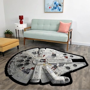 Peut inclure: Un tapis détaillé gris et blanc représentant le Faucon Millenium, avec des bordures noires. Le tapis est de forme circulaire, avec des détails complexes du vaisseau spatial emblématique. Il est posé sur un sol en bois dans un salon.