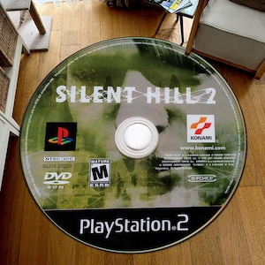 May include: A green and black PlayStation 2 game disc for Silent Hill 2. The disc has a mature rating and is labeled NTSC U/C. The disc is labeled SLUS 20228.