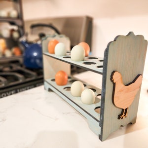 May include: A light blue wooden egg holder with a cutout of a chicken on the side. The holder has two shelves and is filled with white and brown eggs.