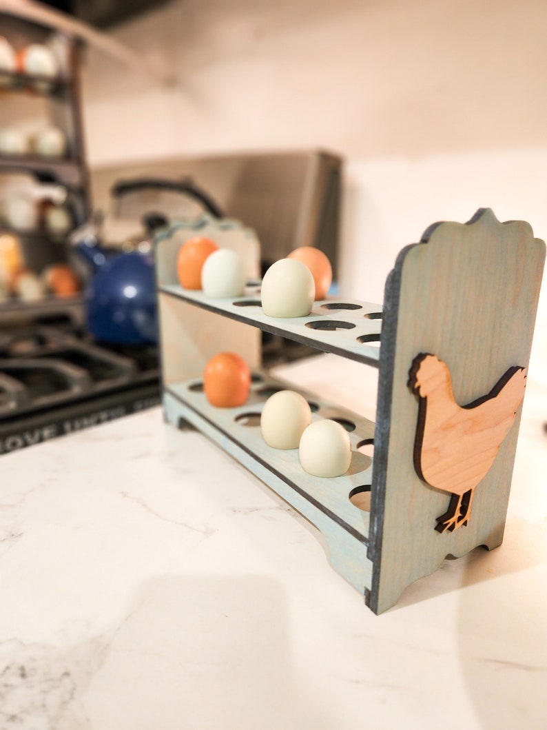 May include: A light blue wooden egg holder with a cutout of a chicken on the side. The holder has two shelves and is filled with white and brown eggs.
