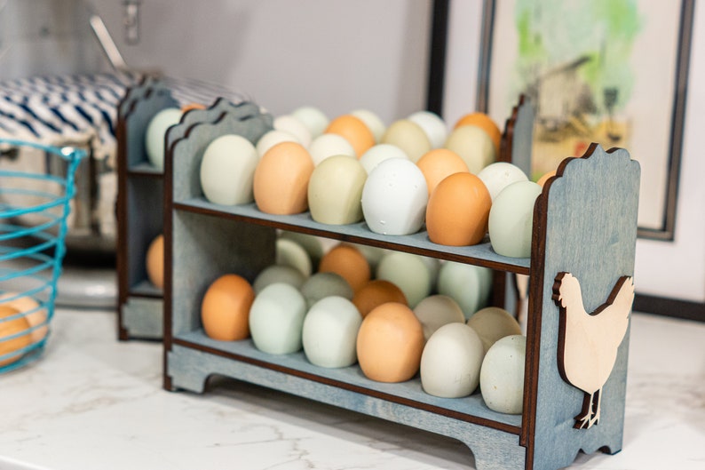 May include: A blue wooden egg holder with two shelves, holding a variety of brown and white eggs. The holder has a cutout of a chicken on the side.