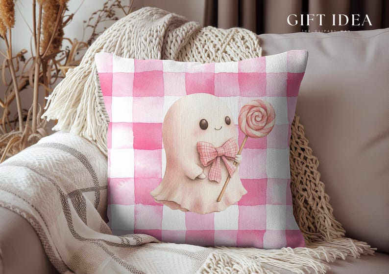 May include: A square decorative pillow with a pink and white gingham pattern. The pillow features a watercolor illustration of a friendly ghost holding a lollipop and wearing a bow. The text "GIFT IDEA" is in the upper right corner.