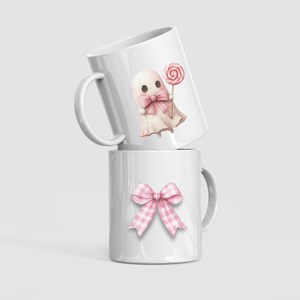 May include: Two white ceramic mugs. One mug features a pink ghost with a bow tie and a lollipop. The other mug has a pink gingham bow. The mugs are stacked on top of each other.
