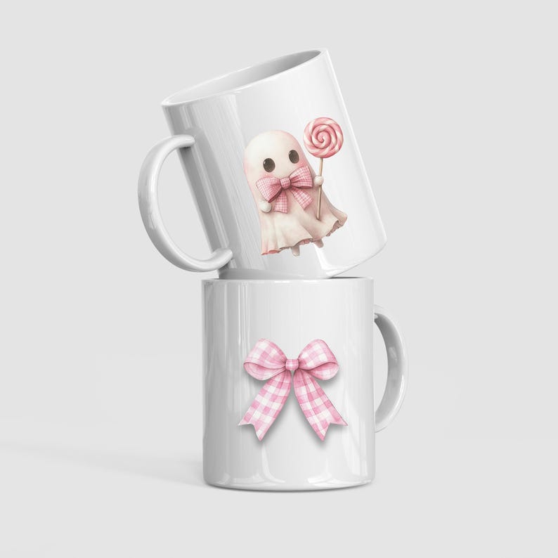 May include: Two white ceramic mugs. One mug features a pink ghost with a bow tie and a lollipop. The other mug has a pink gingham bow. The mugs are stacked on top of each other.