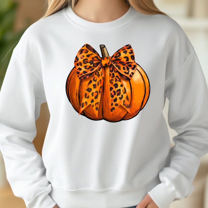 May include: White sweatshirt with a graphic of an orange pumpkin with a leopard print bow.