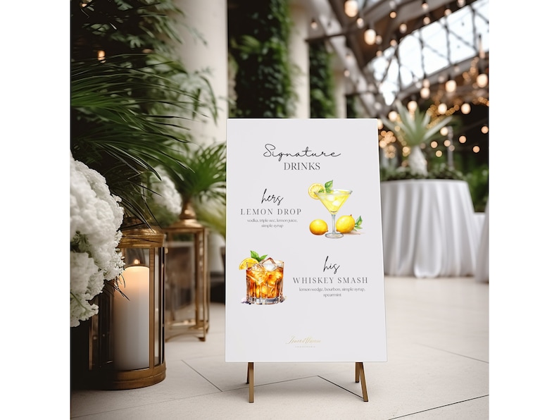 May include: A white sign on a gold easel displays "Signature Drinks" with watercolor illustrations of cocktails. The "hers" drink is a Lemon Drop, and the "his" drink is a Whiskey Smash. The sign is in an elegant setting with candles and greenery.