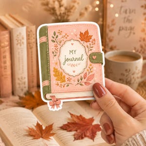 Op de afbeelding: Een gestanste sticker van een lichtroze dagboek met een groene rug en sluiting. Op de kaft staat de tekst MY journal in een decoratief kader, omringd door illustraties van herfstbladeren, kleine bloemen en een klein roze strikje aan de onderkant.