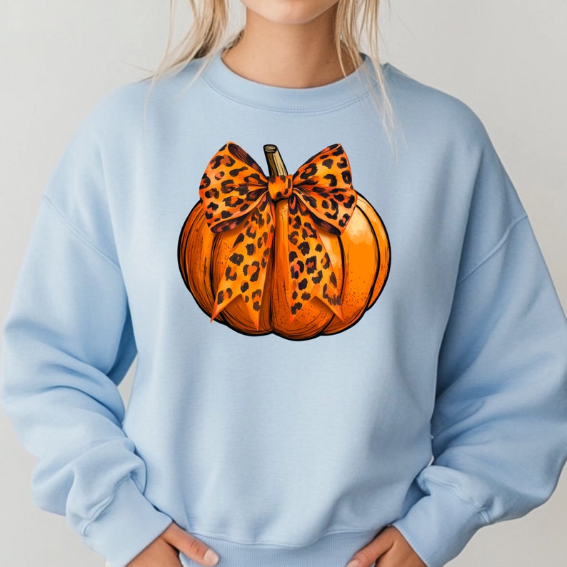 May include: A light blue sweatshirt with a graphic of an orange pumpkin with a leopard print bow.