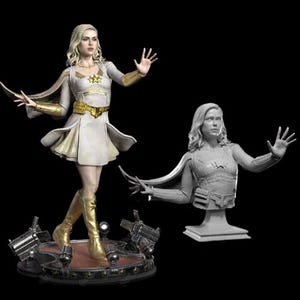 Può includere: Una statua di supereroina bianca e dorata con un mantello e una stella sul petto. La statua è in posa con un braccio alzato e l'altro teso. È anche mostrato un busto separato della stessa supereroina in grigio.
