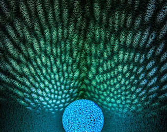 May include: A blue, spherical lamp with a patterned surface casts a green and blue light pattern on the wall behind it.