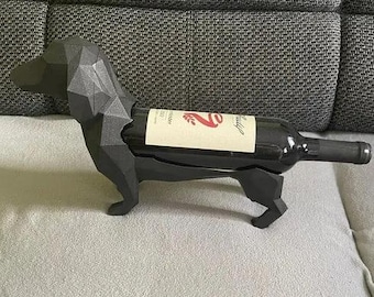May include: A black geometric dachshund-shaped wine bottle holder. The holder is holding a bottle of red wine with a label that reads "Santa Julia" and a red number "2".