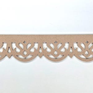 May include: A long, horizontal strip of light brown, unfinished wood featuring a repeating laser-cut decorative pattern. The design consists of a series of interconnected, symmetrical, curved arches and pointed shapes along the bottom edge.