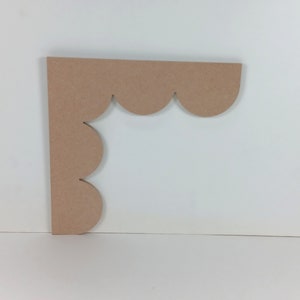 May include: A light brown wooden corner piece with a scalloped edge. The piece is cut in the shape of a right angle.