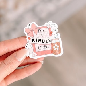 May include: A pink and white sticker with a pink and white bow, a pink book with a white grid pattern, and the text "I'm a Kindle Girlie".